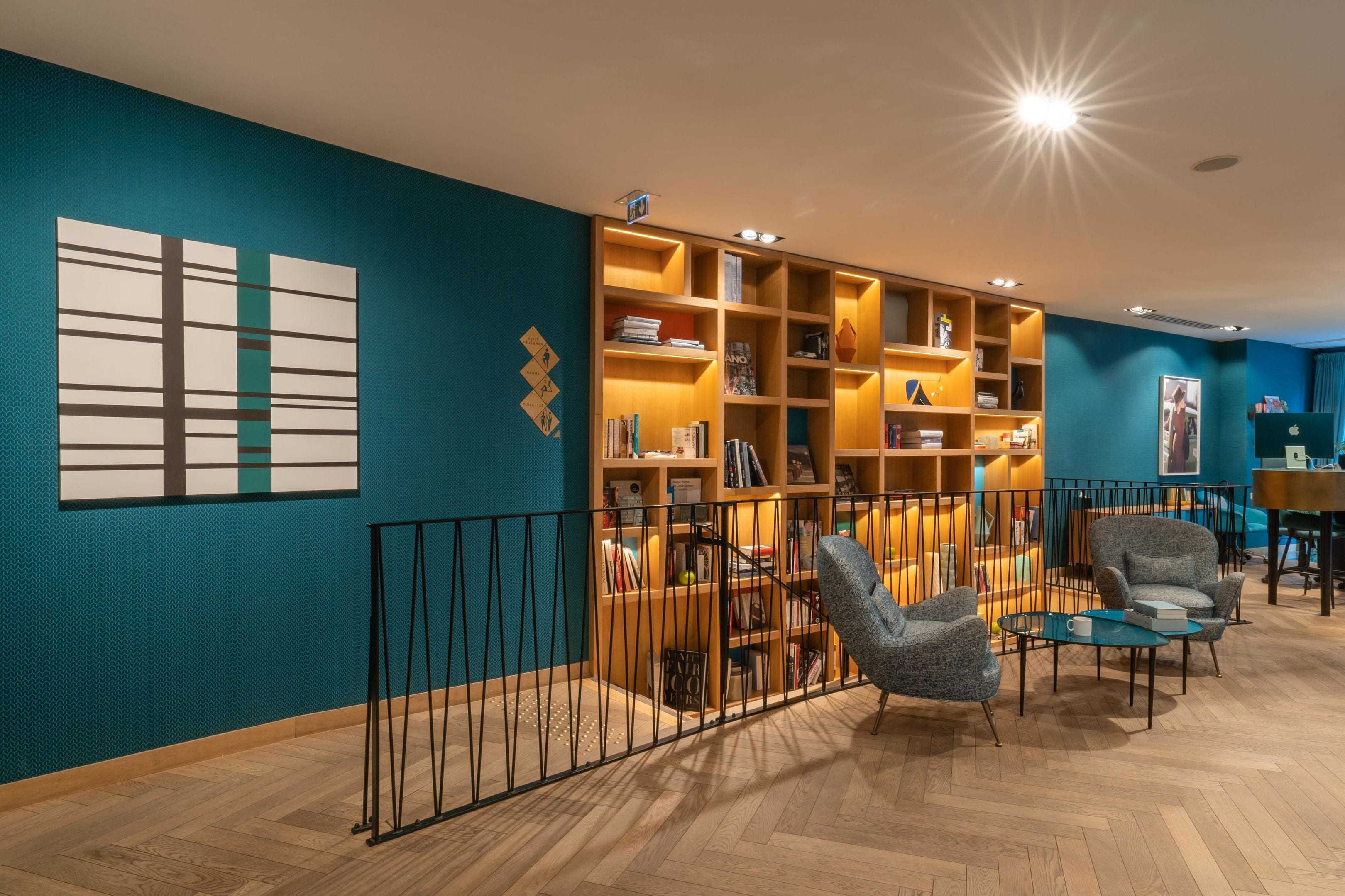 A modern library with wooden bookshelves, comfortable seating, and a teal accent wall.