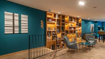 A modern library with wooden bookshelves, comfortable seating, and a teal accent wall.