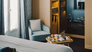 A hotel room with a bed, a small seating area with a chair, a wooden sideboard, and a breakfast tray on the floor. - Hôtel Artus (Paris)