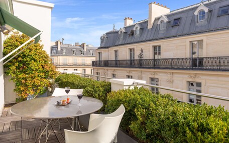A rooftop terrace with a round table, a glass of wine, and a view of Parisian buildings.