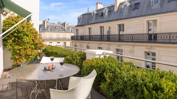 A rooftop terrace with a round table, a glass of wine, and a view of Parisian buildings. - Golden Tulip Opera De Noailles (Paris)