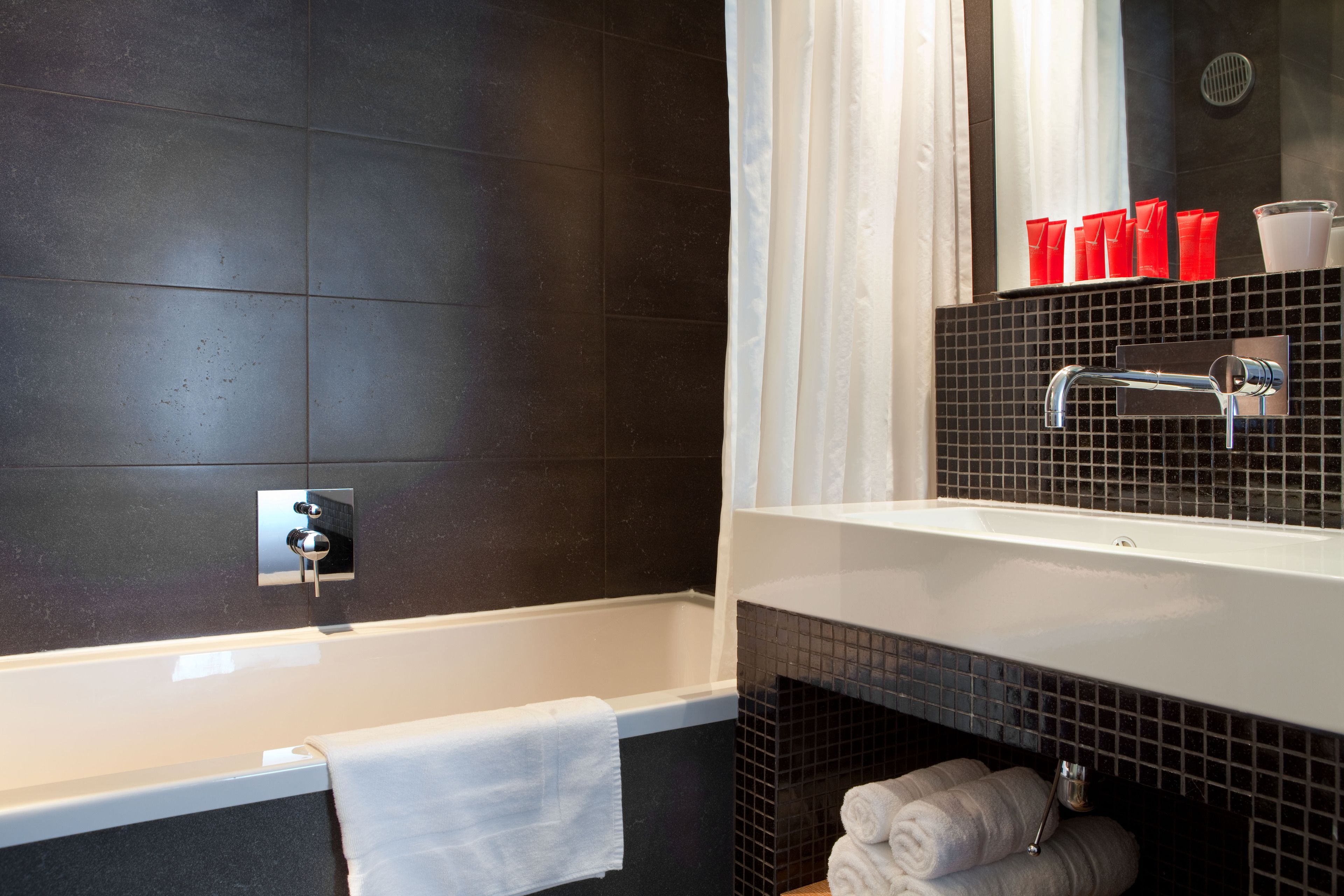 A modern bathroom with a bathtub, a sink with a mirror above it, and a tiled backsplash.