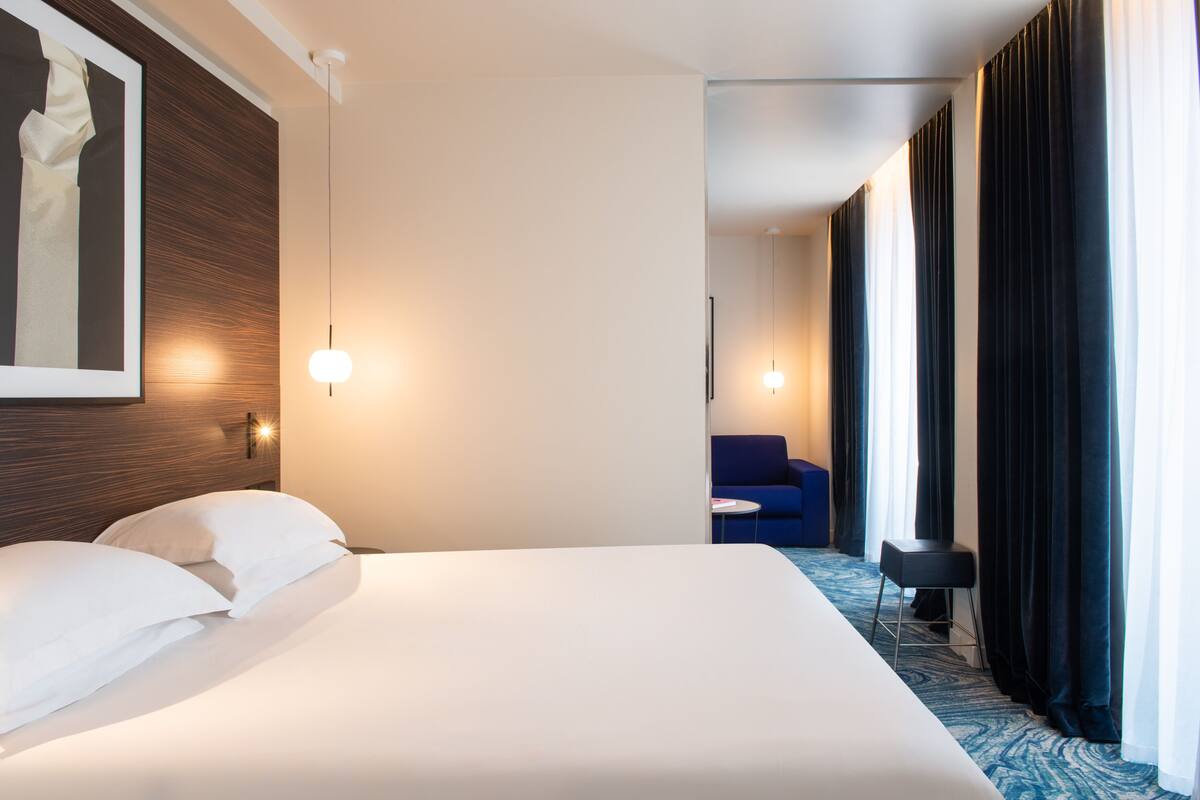 A hotel room with a large bed, a desk, a chair, and a view of the city.
