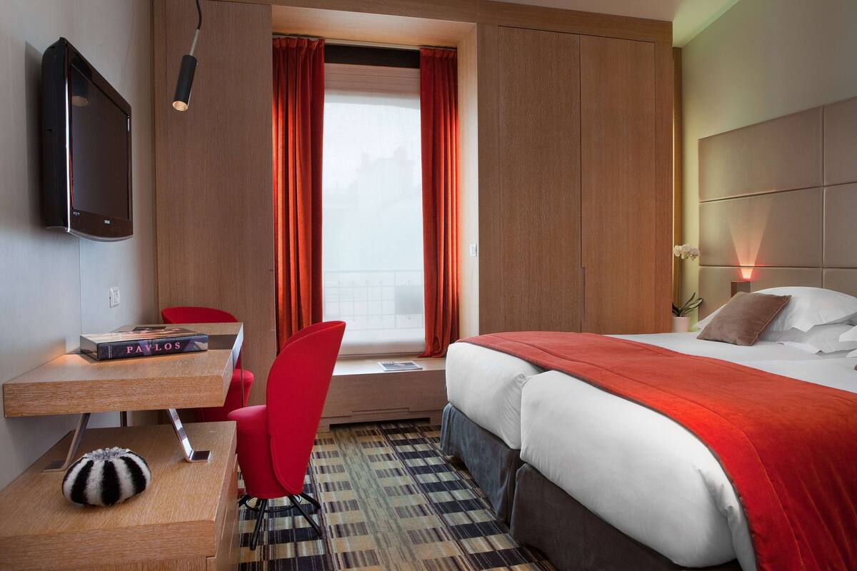 A hotel room with a bed, a desk, a chair, a television, and a window with curtains.