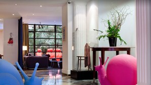 A spacious lobby with a large window, a potted plant, and a seating area with a sofa and chairs. - Golden Tulip Opera De Noailles (Paris)