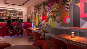 A bar area with stools, a bar counter, and a mural with tropical and abstract designs. - Golden Tulip Opera De Noailles (Paris)