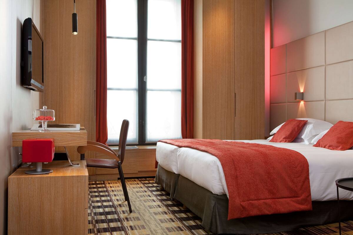 A hotel room with a bed, a desk with a chair, a television, and a window with curtains.