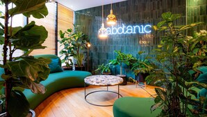 A modern interior with a curved green sofa, a round coffee table, and various potted plants. - Mercure Paris Montparnasse Pasteur (Paris)