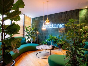 A modern interior with a curved green sofa, a round coffee table, and various potted plants. - Mercure Paris Montparnasse Pasteur (Paris)