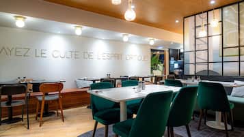 Et restaurantinteriør med moderne design, med trælofter, grønne polstrede stole og en væg med restaurantens navn.