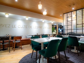 A restaurant interior with a modern design, featuring wooden ceiling panels, green upholstered chairs, and a wall with the restaurant's name. - Mercure Paris Montparnasse Pasteur (Paris)