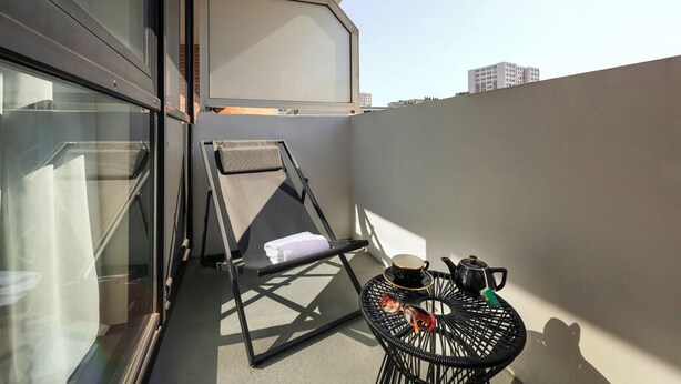 A balcony with a chair, a small round table with a cup and a teapot, and a view of the cityscape. - Mercure Paris Montparnasse Pasteur (Paris)