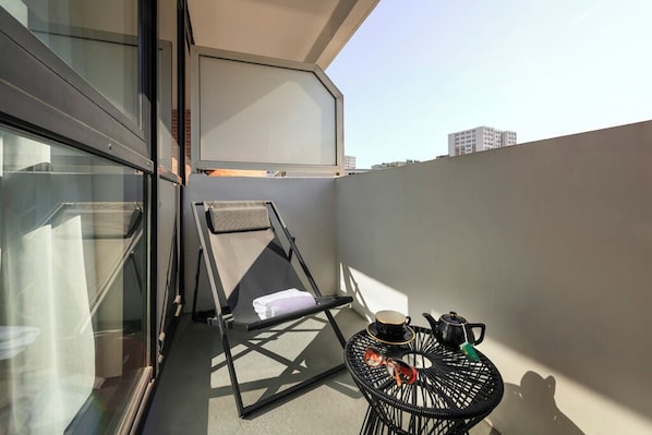 A balcony with a chair, a small round table with a cup and a teapot, and a view of the cityscape. - Mercure Paris Montparnasse Pasteur (Paris)