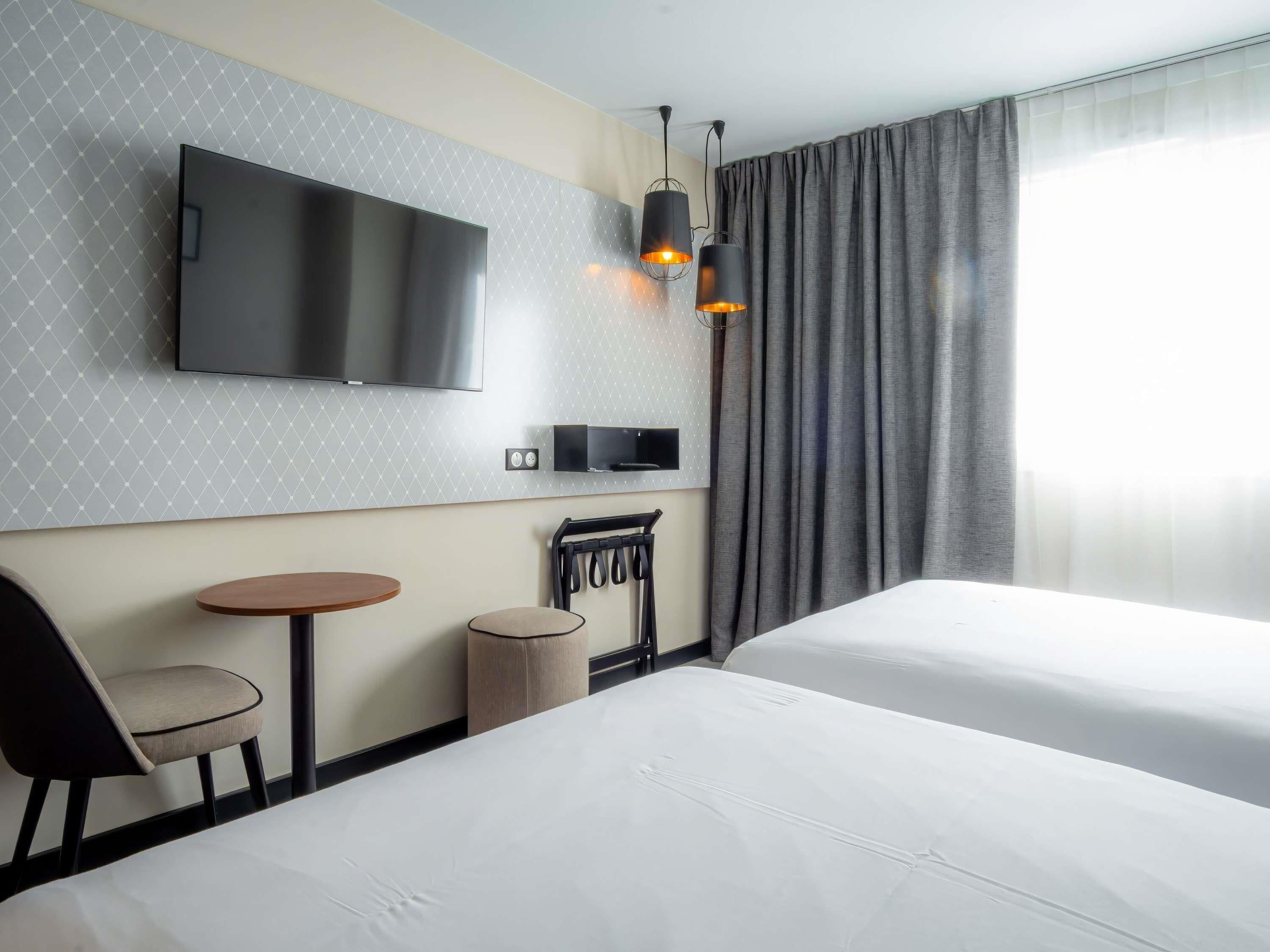 Habitación de hotel con dos camas, televisor, una mesita, una silla y una lámpara.