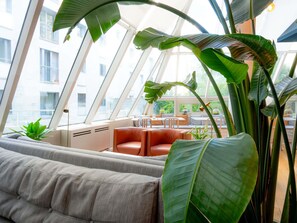 A modern interior with a sofa, a dining area, and large green plants. - Mercure Paris Montparnasse Pasteur (Paris)