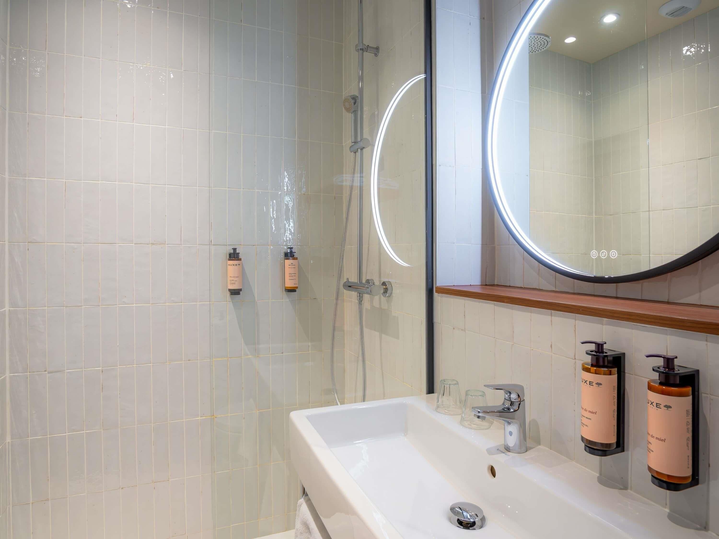 Un baño moderno con cabina de ducha de vidrio, un lavamanos blanco con espejo y dos artículos de tocador sujetos a la pared.