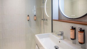 A modern bathroom with a glass shower enclosure, a white sink with a mirror above it, and two toiletries mounted on the wall. - Mercure Paris Montparnasse Pasteur (Paris)