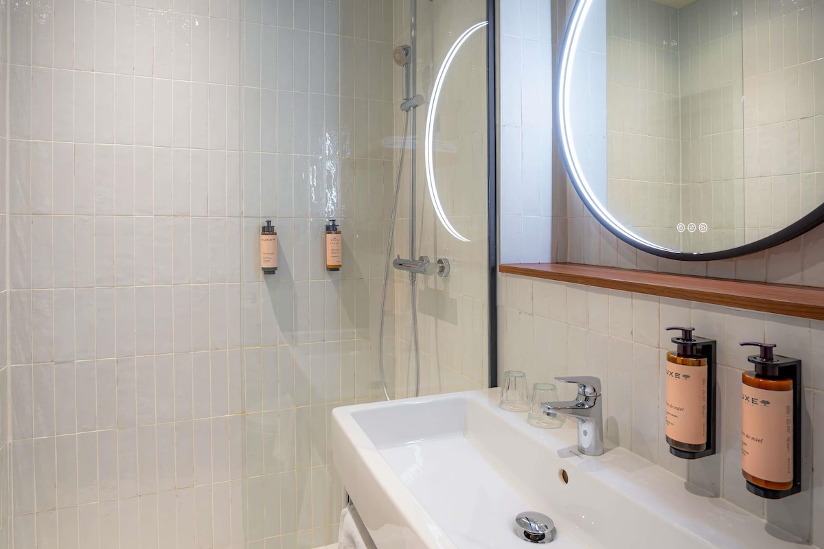 A modern bathroom with a glass shower enclosure, a white sink with a mirror above it, and two toiletries mounted on the wall.