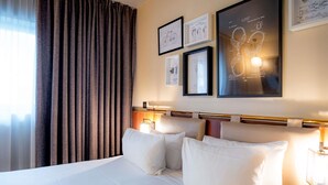 A hotel room with a large bed, a headboard with a light fixture, and framed drawings on the wall. - Mercure Paris Montparnasse Pasteur (Paris)