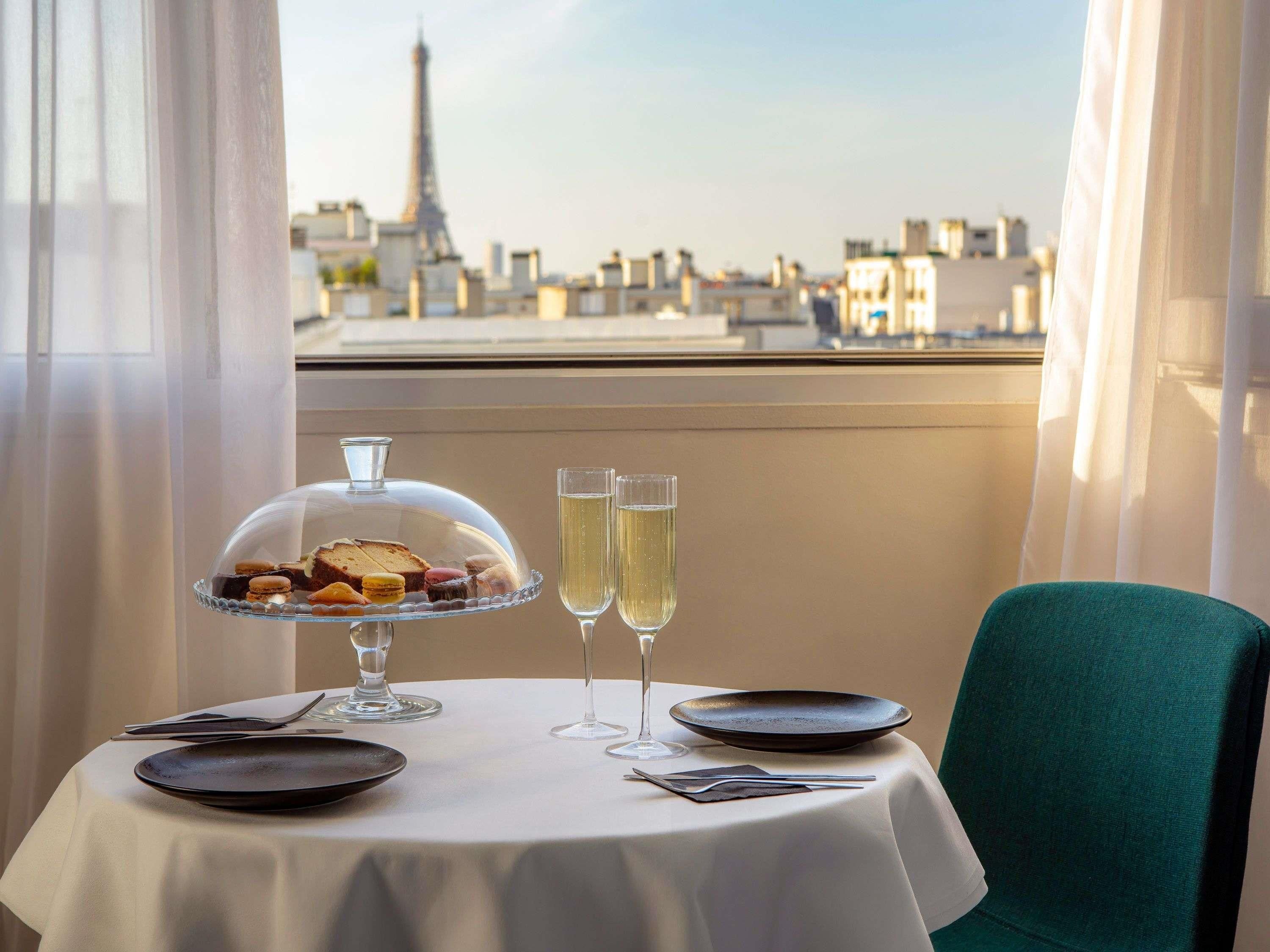 A table set for two with a dessert display, two glasses of champagne, and a view of the Eiffel Tower.