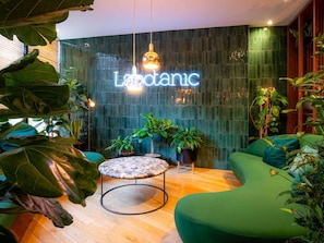 A modern interior with a neon sign, round table, green seating, and potted plants. - Mercure Paris Montparnasse Pasteur (Paris)