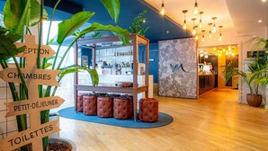 A hotel lobby with a reception desk, directional signs, a seating area, and a bar. - Mercure Paris Montparnasse Pasteur (Paris)