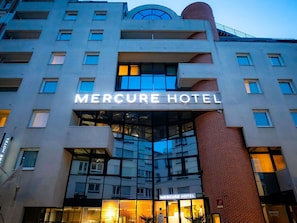 L'esterno dell'Hotel Mercure, caratterizzato da un design architettonico moderno, con ampie vetrate e un ingresso ben visibile.