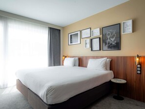 Una habitación de hotel con una cama grande, una mesita de noche, una lámpara de pared y cuadros enmarcados.