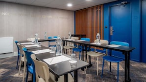 A conference room with tables and chairs, a whiteboard, and a blue wall with a vertical wooden panel. - Mercure Paris Montparnasse Pasteur (Paris)