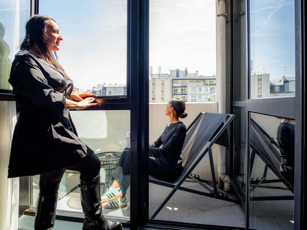 A person standing by a window with a view of buildings and a chair outside. - Mercure Paris Montparnasse Pasteur (Paris)