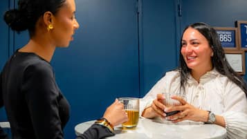 Dos personas sentadas en una mesa redonda en una habitación con paredes azules, sosteniendo vasos de cerveza.
