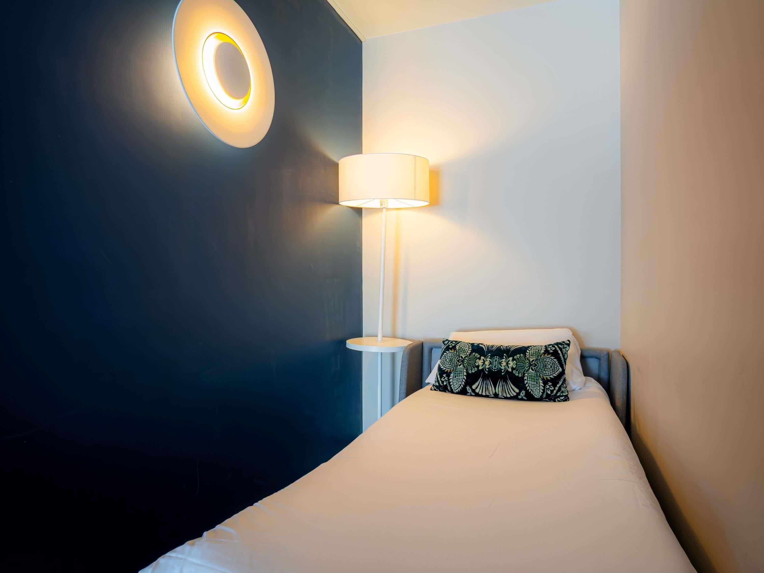 Une chambre d’hôtel avec un lit, une lampe de chevet et un luminaire fixé au mur.