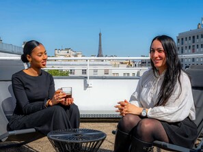Two people sitting on a rooftop terrace with a view of a cityscape and a tower in the background. - Mercure Paris Montparnasse Pasteur (Paris)