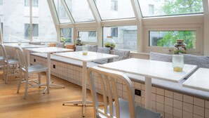 A modern interior with high ceilings, large windows, and a mix of seating options including tables and benches. - Mercure Paris Montparnasse Pasteur (Paris)