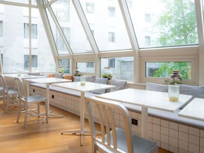 A modern interior with high ceilings, large windows, and a mix of seating options including tables and benches.