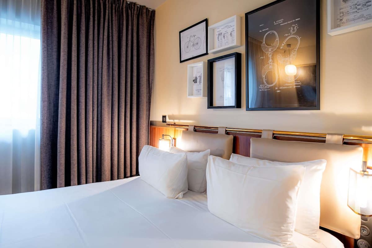 A hotel room with a large bed, a headboard with a light fixture, and framed drawings on the wall.