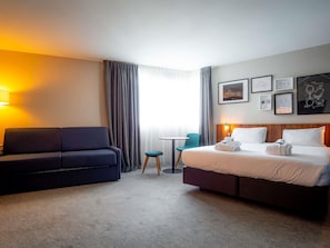 A hotel room with a bed, a sofa, a small table, and a chair. There are curtains, a lamp, and framed pictures on the wall. - Mercure Paris Montparnasse Pasteur (Paris)