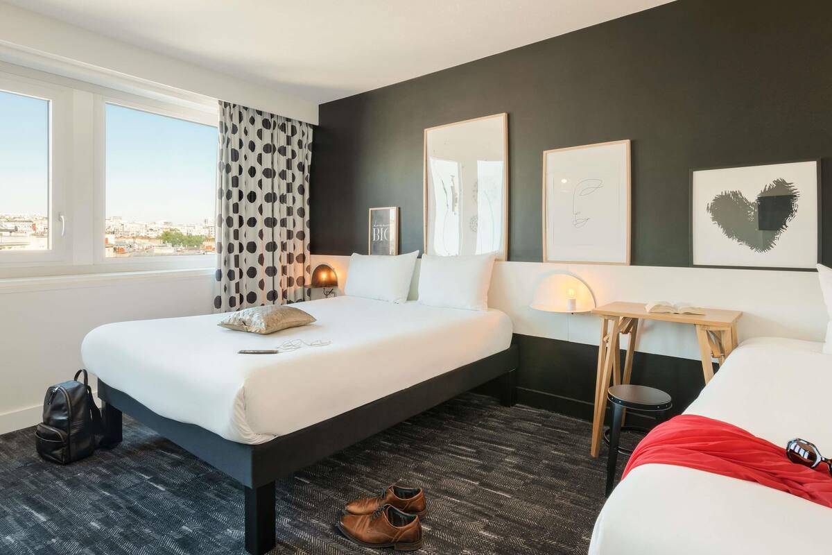 Hotellihuone, jossa on sänky, yöpöytä, lamppu ja näkymä kaupunkiin.