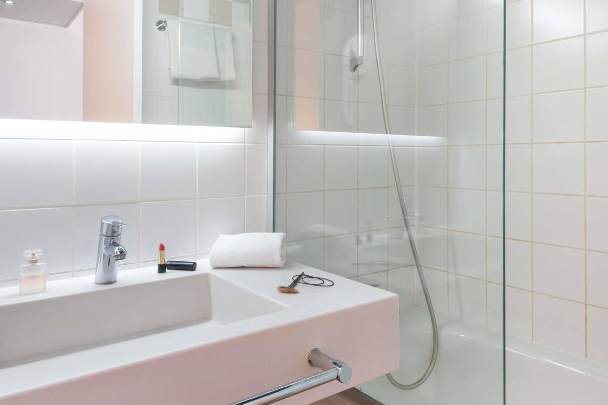 Moderni kylpyhuone, jossa on lasinen suihkuseinä, valkoinen pesuallas, jonka yläpuolella on peili, ja pyyhe, joka on ripustettu seinälle.