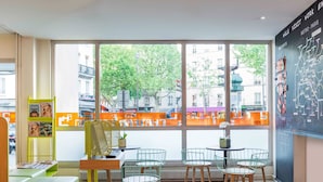 A modern cafe with large windows, a blackboard with maps, and a yellow bookshelf. - ibis Styles Paris Gare de l'Est Château Landon (Paris)