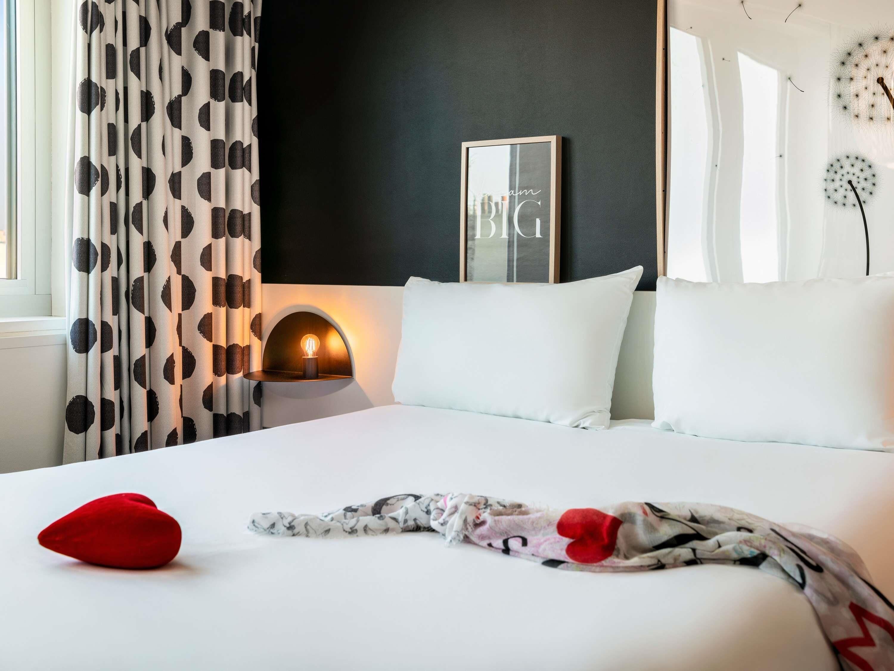 Una camera da letto con un letto, una lampada da comodino, una sveglia a parete e una finestra con tende.
