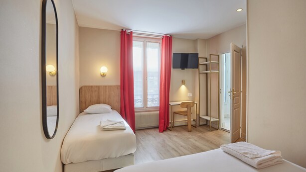 Une chambre d’hôtel avec deux lits, un bureau, une chaise, une télévision et une fenêtre avec des rideaux.