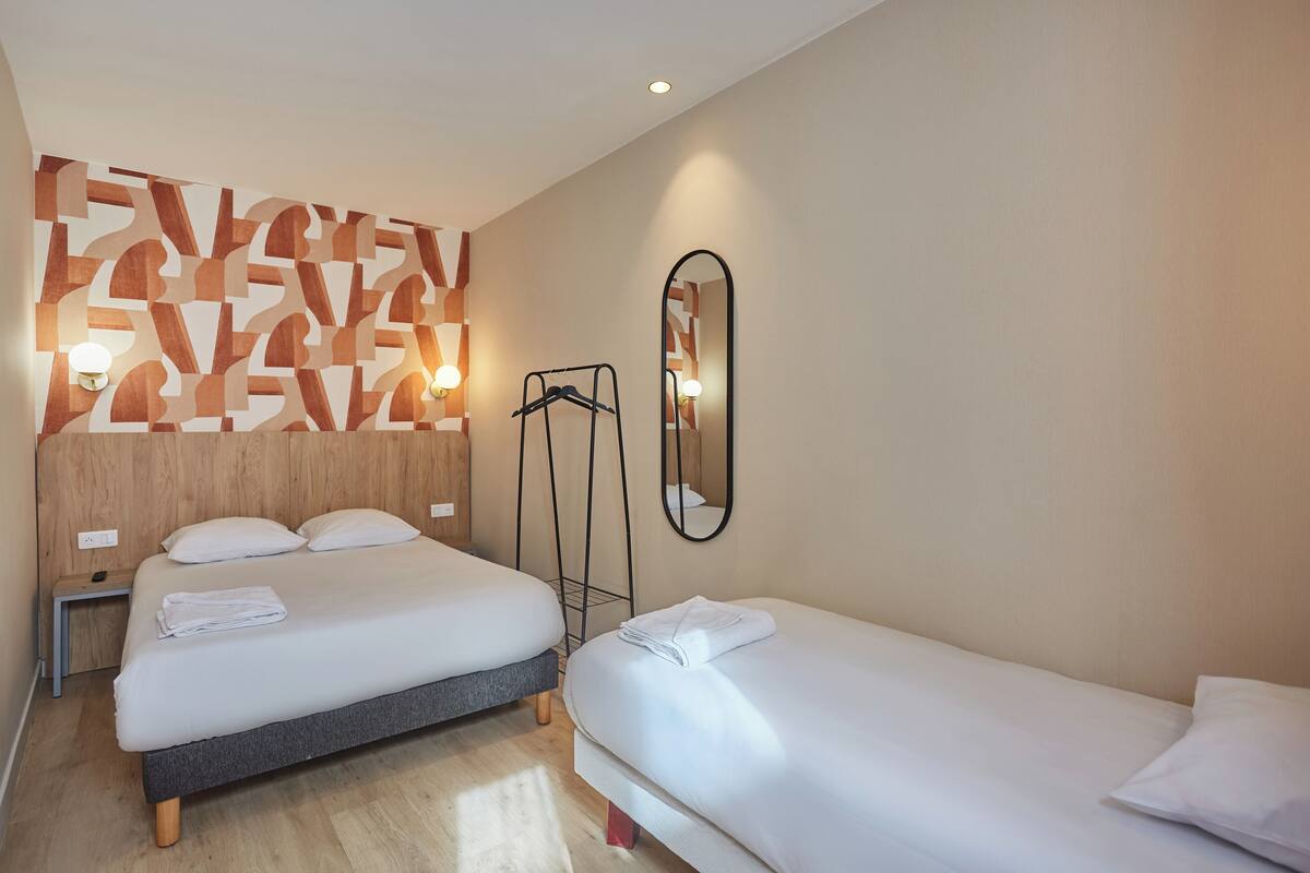 A hotel room with two beds, a wooden headboard, a mirror, and a wall-mounted light fixture.