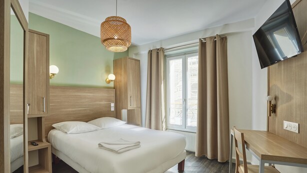 Habitación de hotel con cama, escritorio, televisor y ventana con cortinas.