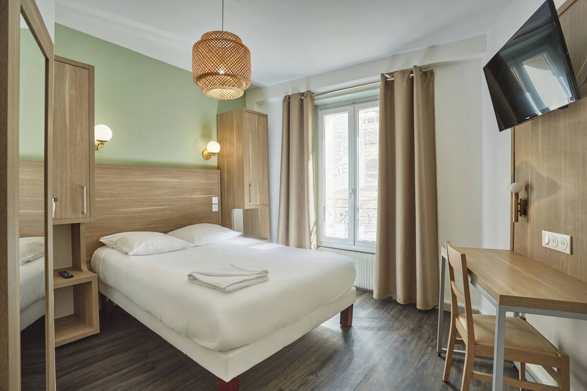 A hotel room with a bed, a desk, a television, and a window with curtains.