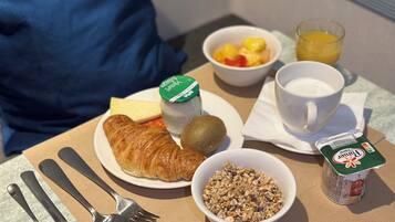 Bandeja de desayuno con croissant, kiwi, yogur, granola, zumo de naranja y una taza de café.