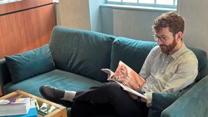 Una persona sentada en un sofá color turquesa leyendo una revista.