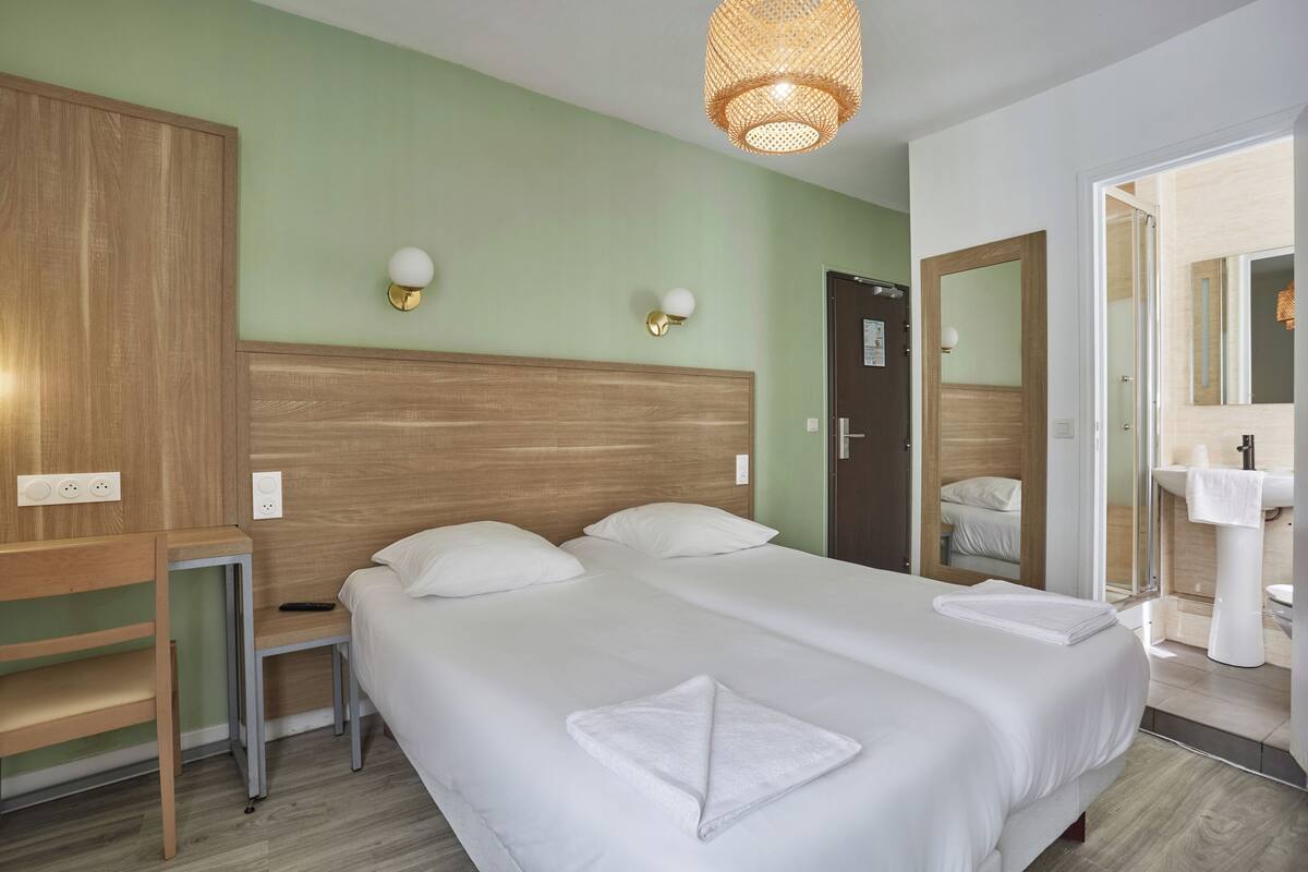 A hotel room with two beds, a wooden headboard, a small table, and a mirror.