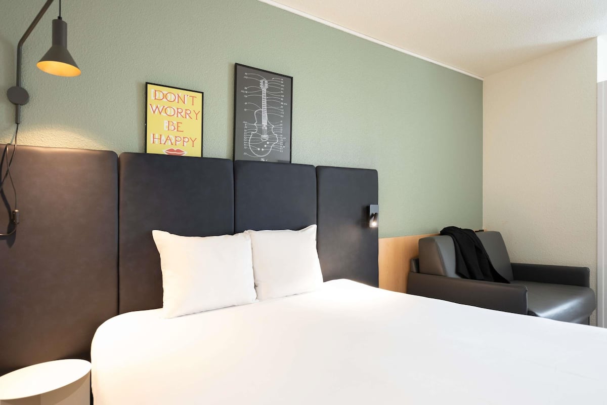 A hotel room with a large bed, a headboard with a motivational quote, a side table, a lamp, and a chair.