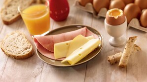 Desayuno con pan, huevos, queso y un vaso de jugo de naranja sobre una mesa de madera.